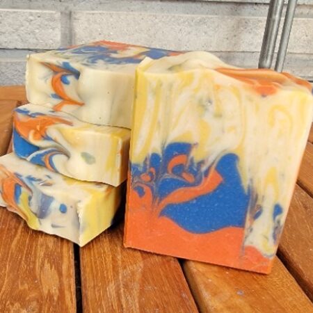 Handmade bar soap with orange, blue, and cream swirls sitting on wood table