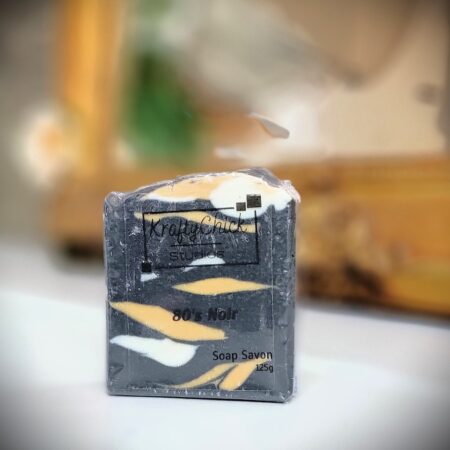 Bar of handmade soap in front of gold mirror. Soap is black, white and gold in a camouflage-like pattern