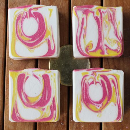 4 bars of handcrafted soap on a wood board. Soap is coloured with white, hot pink, and yellow swirls.