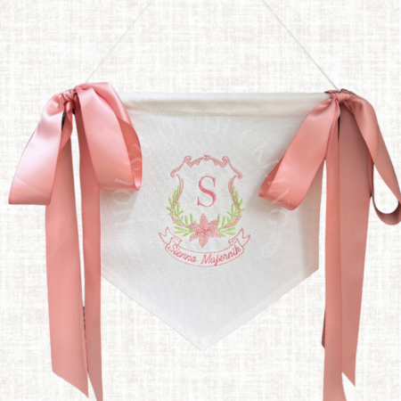 A close-up of a personalized embroidered baby banner, featuring delicate stitching of the baby’s name and initial, hung on a wooden dowel.