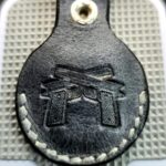 Gray leather Apple AirTag case with guns stamped into it.