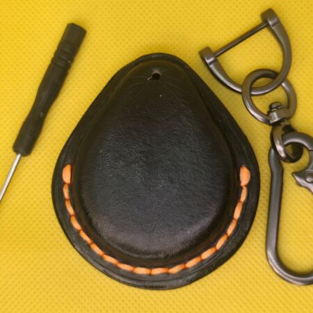 Back view of a Black veg-tanned leather key fob case for Harley Davidson motorcycles with orange stitching next to a solid stainless steel lobster clasp keychain and mini screwdriver.