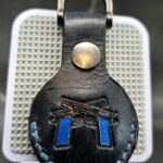 Black leather Apple AirTag holder stamped with a pair of navy handled guns with blue stitching