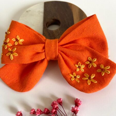 Hand-embroidered apricot linen bow with pastel floral details from Thread & Stitch Studio.