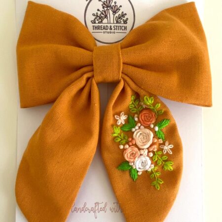 Mustard oversized bow with orange and green floral details, photographed on a light surface.