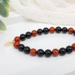 Red jasper and black onyx beaded stretch bracelet with 14K gold-filled square accent beads and a 14K gold-filled feather charm centerpiece.
