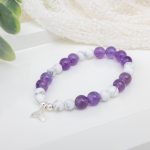 Stretch bracelet of smooth white howlite and faceted amethyst beads centered by a sterling silver mermaid tail charm on elastic cord.