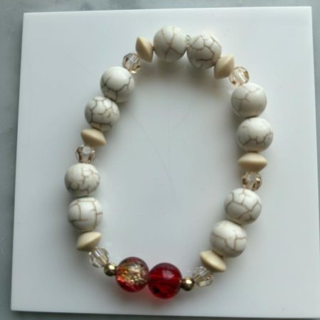 Stretch bracelet of white turquoise beads with golden Swarovski accents, 14K gold‑filled spacer beads, and red‑yellow crackle centerpiece beads.