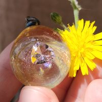 Handmade round glass pendant featuring a pink crystal suspended inside.